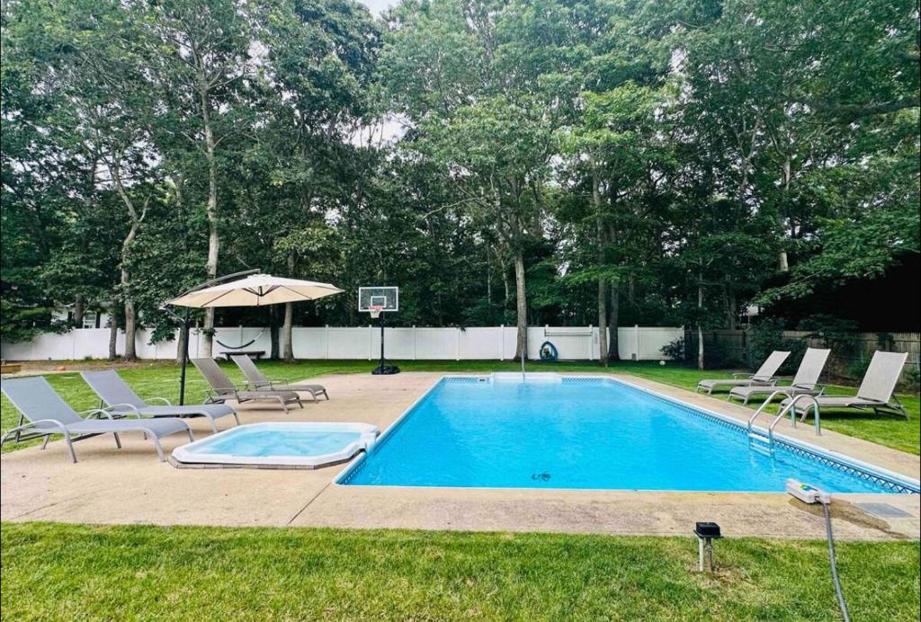 una piscina con sillas, una sombrilla y un aro de baloncesto en Hampton's Getaway w/ pool, en East Hampton