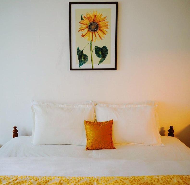 een bed met witte kussens en een foto van een zonnebloem bij Fortis Rooms in Cochin