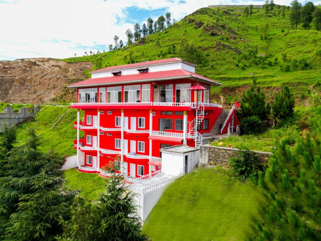 a red house on a hill with a green hillside at RED ROSE HOTEL & RESORT Mansehra in Mānsehra