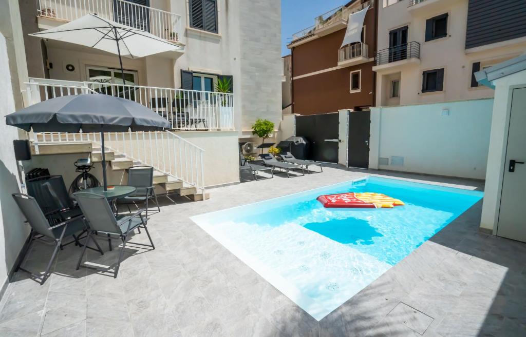 una piscina con tavolo, sedie e ombrellone di Scirocco Holiday House DIAMANTE a Rosolini