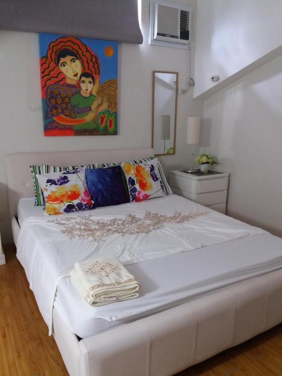 uma cama branca num quarto com uma pintura na parede em Beautiful condo with WIFI and pool near Nuvali em Cavite