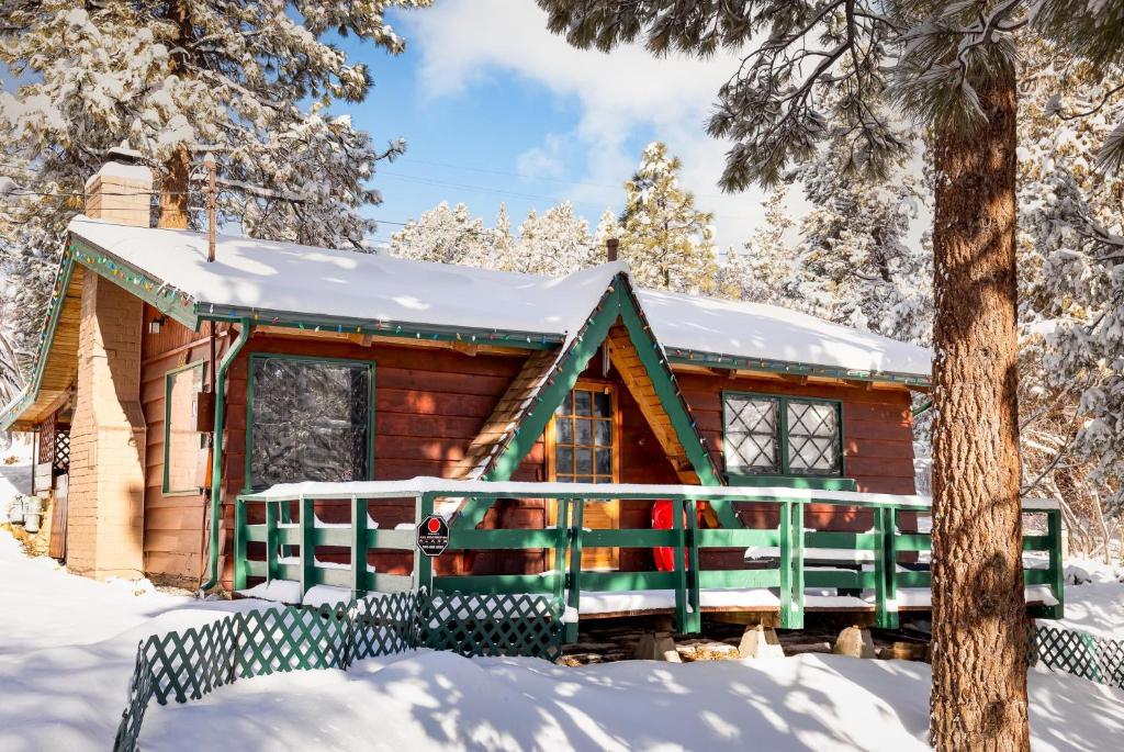 una cabaña de madera en la nieve con una barandilla verde en 056 - Beaumont Hideaway, en Big Bear City