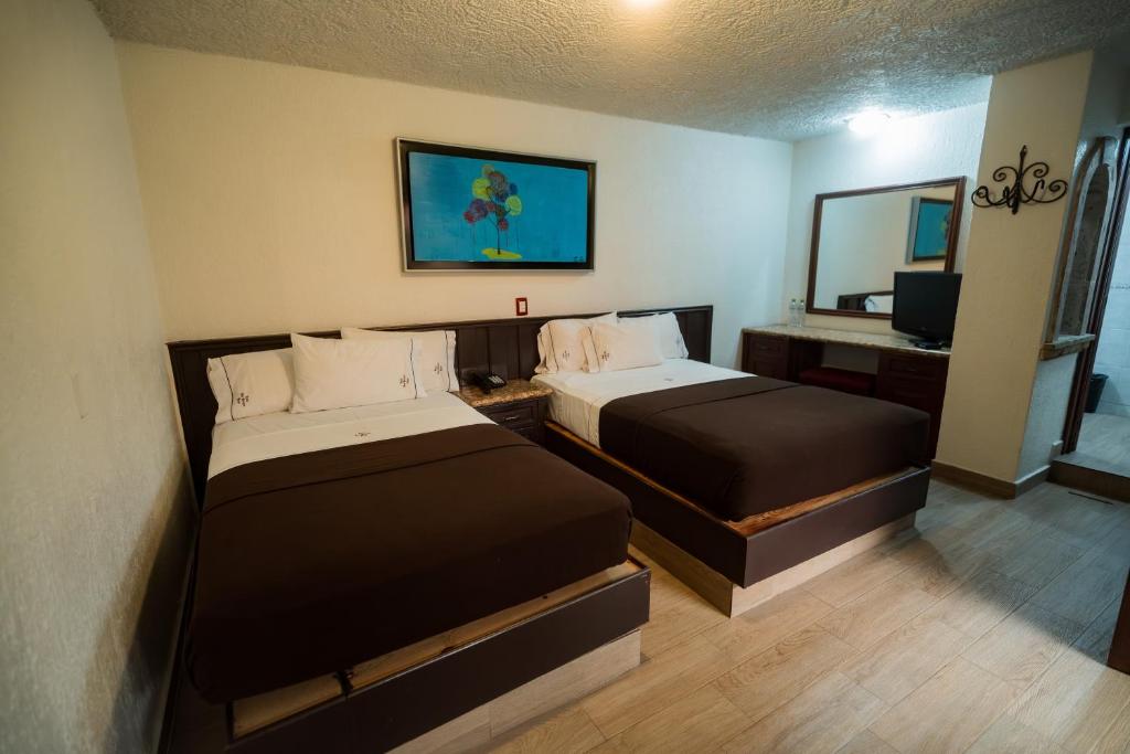 a hotel room with two beds and a mirror at Hotel Don Quijote Plaza - Guadalajara Centro Historico in Guadalajara
