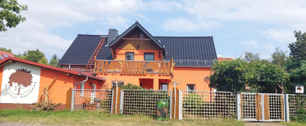 an orange house with a black roof behind a fence at Wildholz Sachsen in Weidenhain