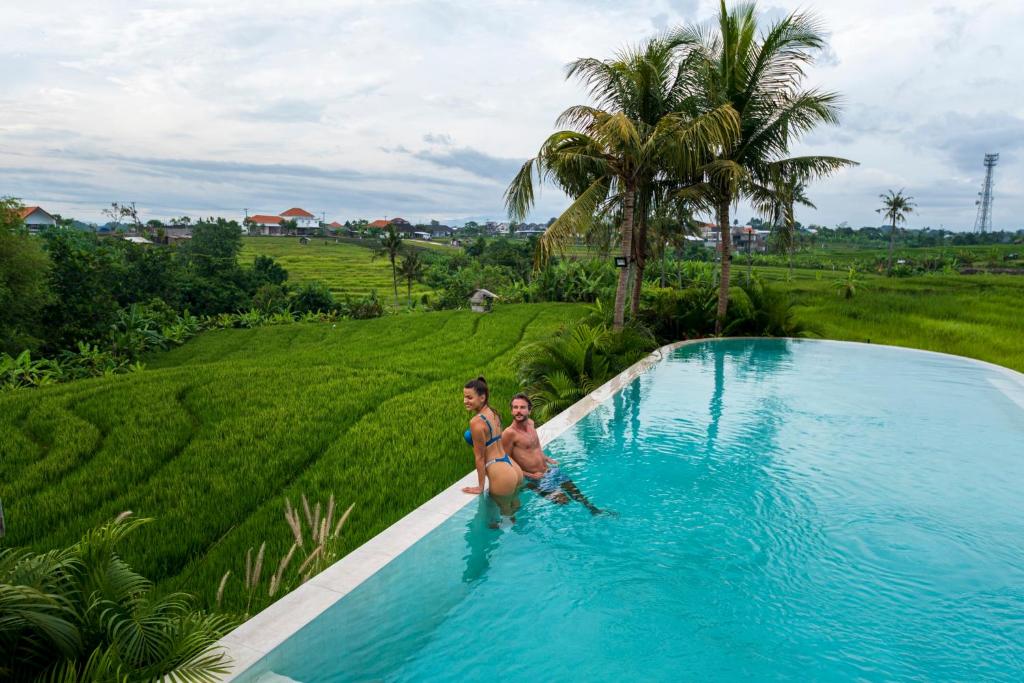 2 personnes debout dans une piscine à côté d'un champ dans l'établissement Astera Resort Canggu by Ini Vie Hospitality, à Canggu