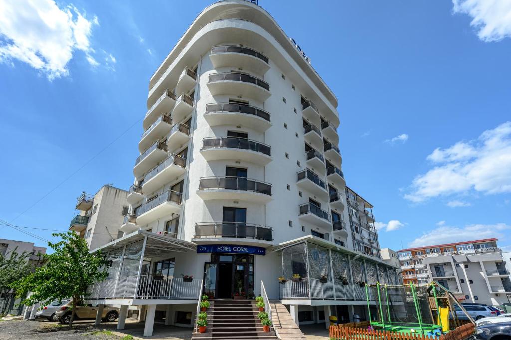 a tall white building with a staircase in front of it at Hotel Coral in Eforie Nord