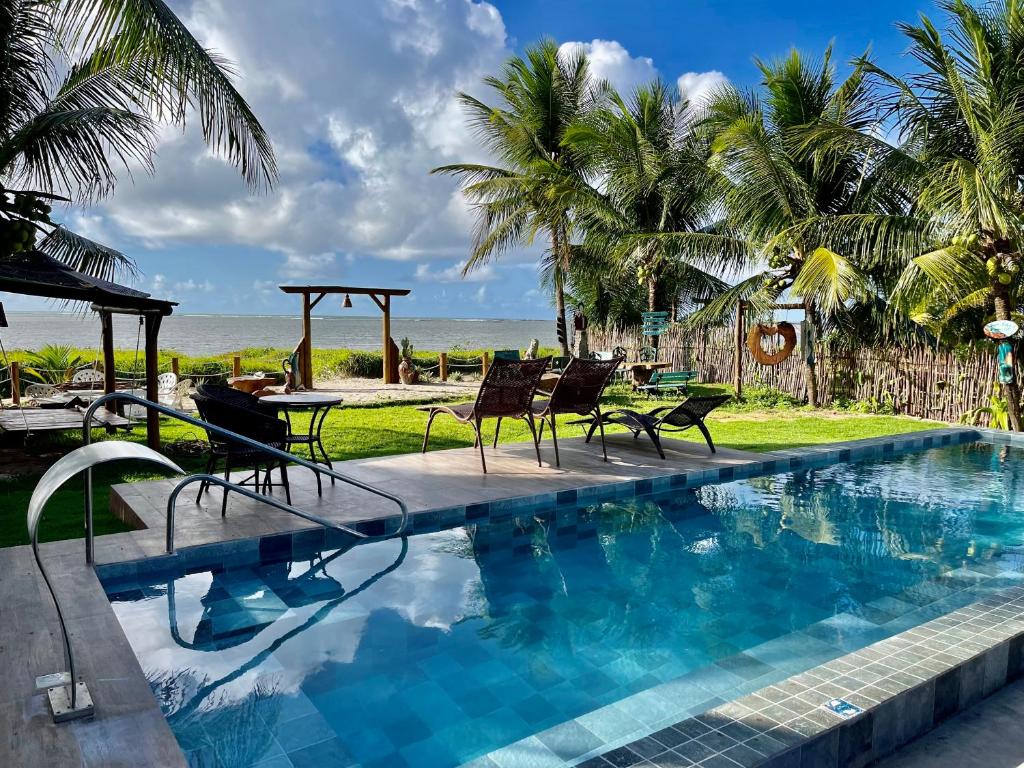 a swimming pool with chairs and a table and the beach at JaParaíso Pousada Ateliê in Japaratinga