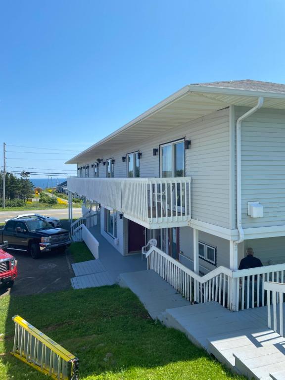 a house with a balcony and a car parked in a parking lot at Hotel-Motel Le Panorama in Perce