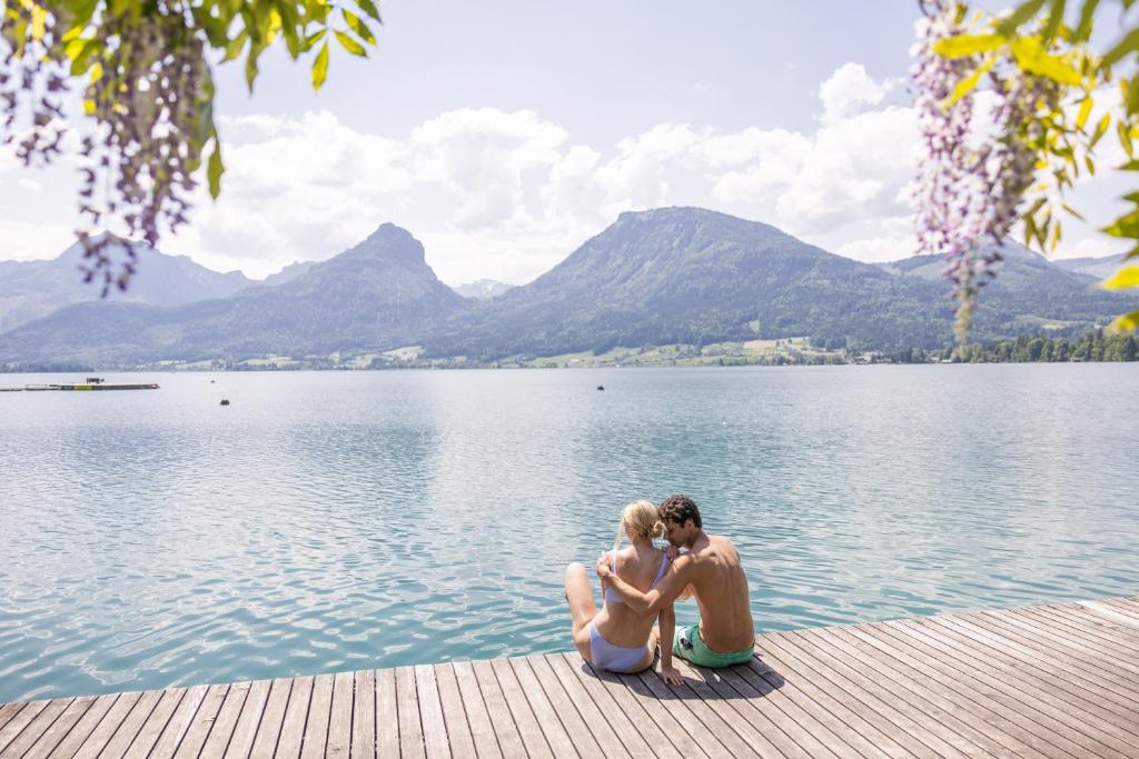 a man and a woman sitting on a dock by a lake at Hotel Seevilla Wolfgangsee in St. Wolfgang