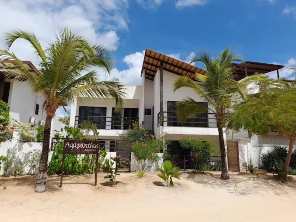 a building on the beach with two palm trees at Agapanthus Apartamentos in Jericoacoara