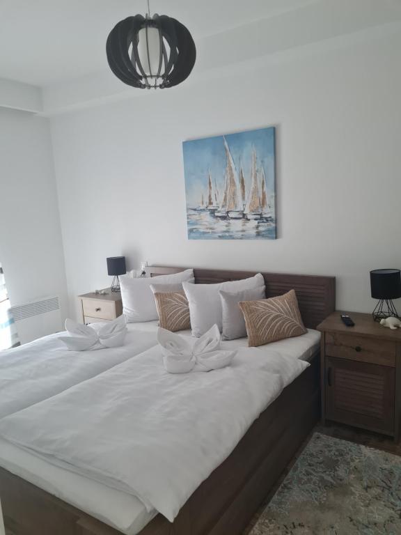 a large bed with white sheets and a painting on the wall at Elina Apartman in Keszthely