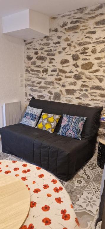 a black couch in a living room with a stone wall at L'arbre dort studio indépendant in Taupont