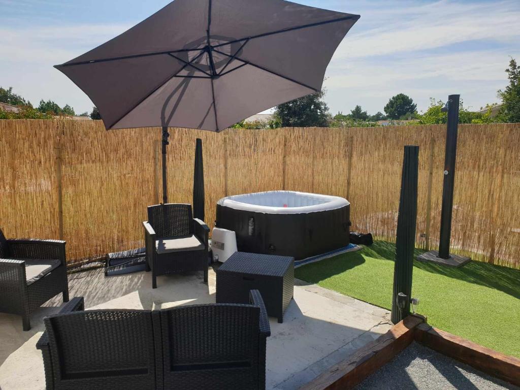 un patio con bañera de hidromasaje y sombrilla en Beau logement avec terrasse, jacuzzi et terrain de pétanque privatif à 5 minutes de la plage en Audenge