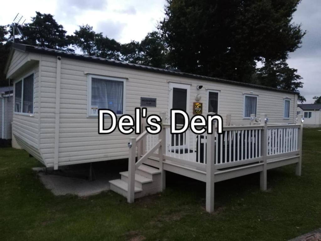 a white trailer with a porch and the words delis den at Del's den lakeside weeley bridge in Weeley