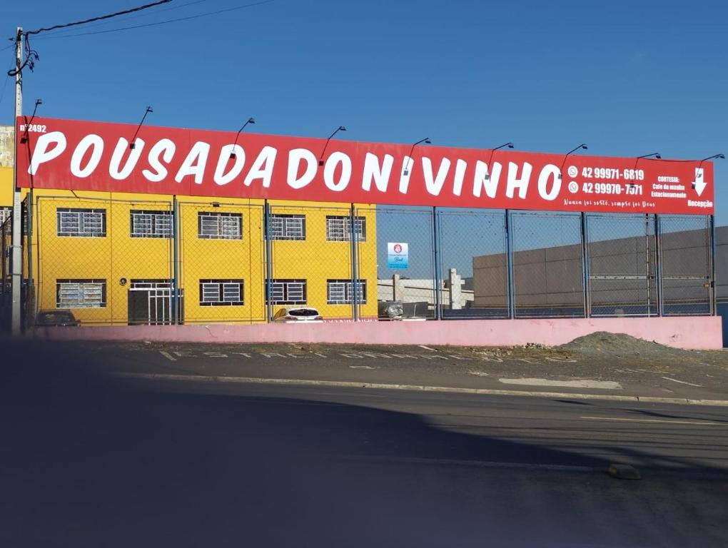 a yellow building with a red and white sign on it at POUSADA DO NIVINHO in Ponta Grossa