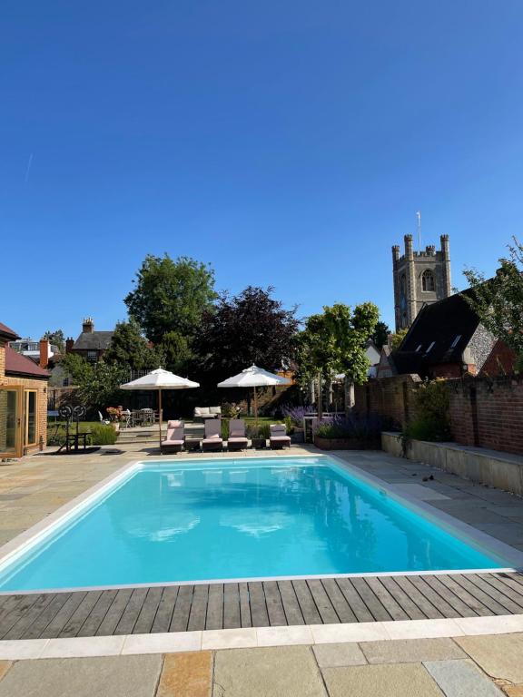une piscine avec des chaises et une église en arrière-plan dans l'établissement The Pool House, à Henley-on-Thames