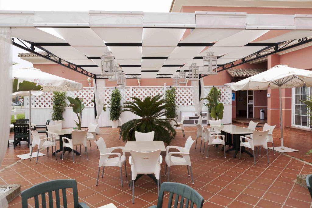 un patio con mesas y sillas blancas y sombrillas blancas en Hostal Rte. Casa Miguel, en Matalascañas