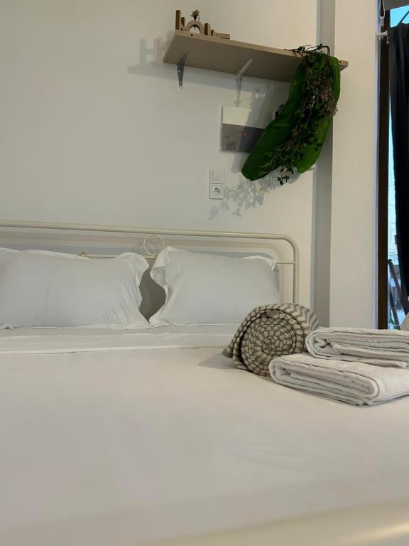ein weißes Bett mit weißen Kissen und einer Pflanze an der Wand in der Unterkunft Paola’s apartments near Athens Airport in Spáta