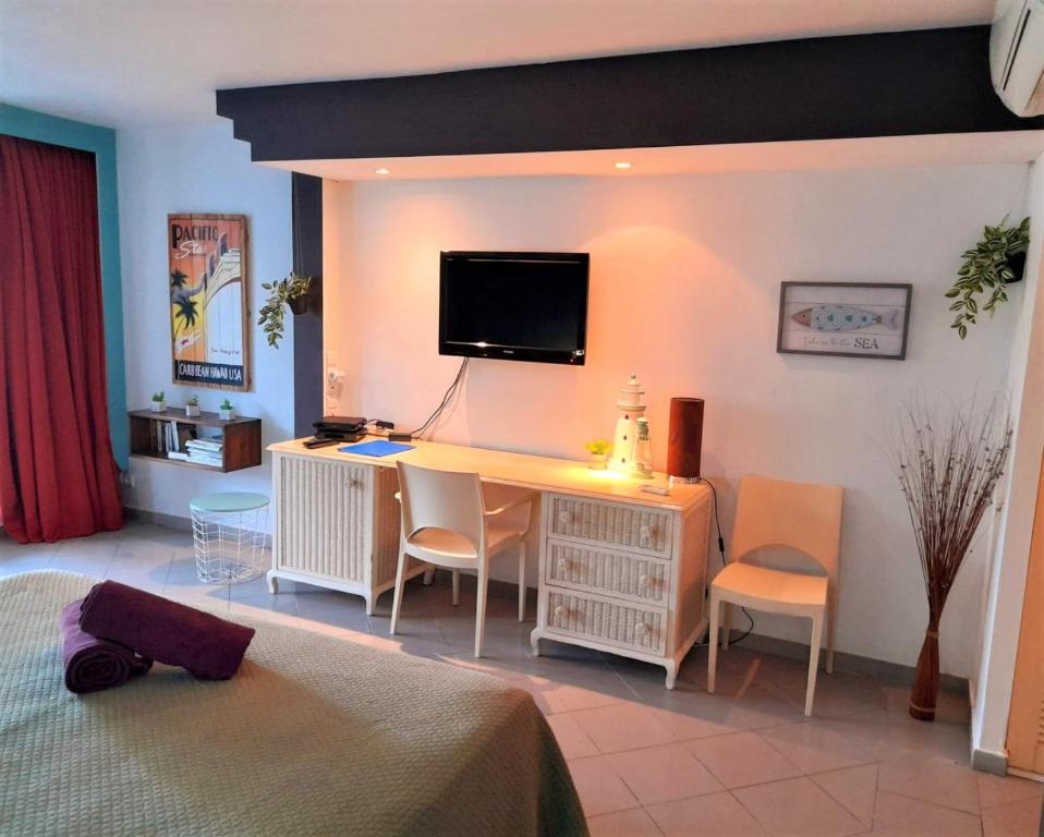 a bedroom with a desk with a television on the wall at ILET BLEU studio cosy RDC vue mer et jardin - Accès direct plage in Le Gosier