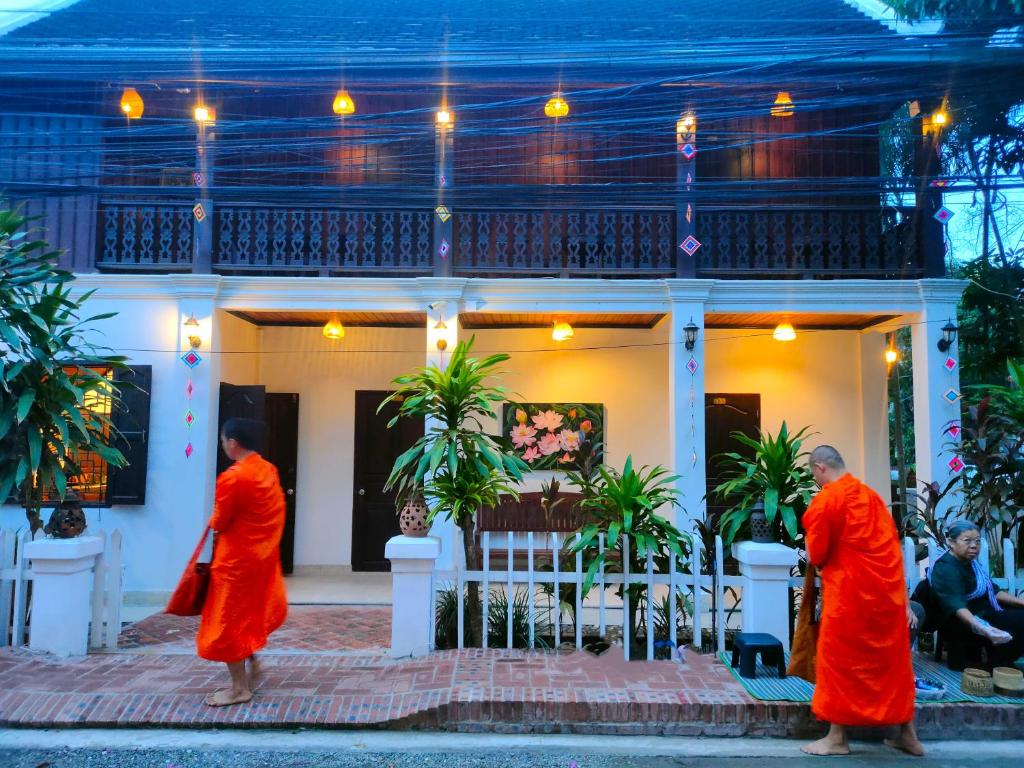 trzech mnichów w pomarańczowych szatach stojących przed domem w obiekcie Lotus Corner - Vegan & Plant Based B&B w mieście Luang Prabang