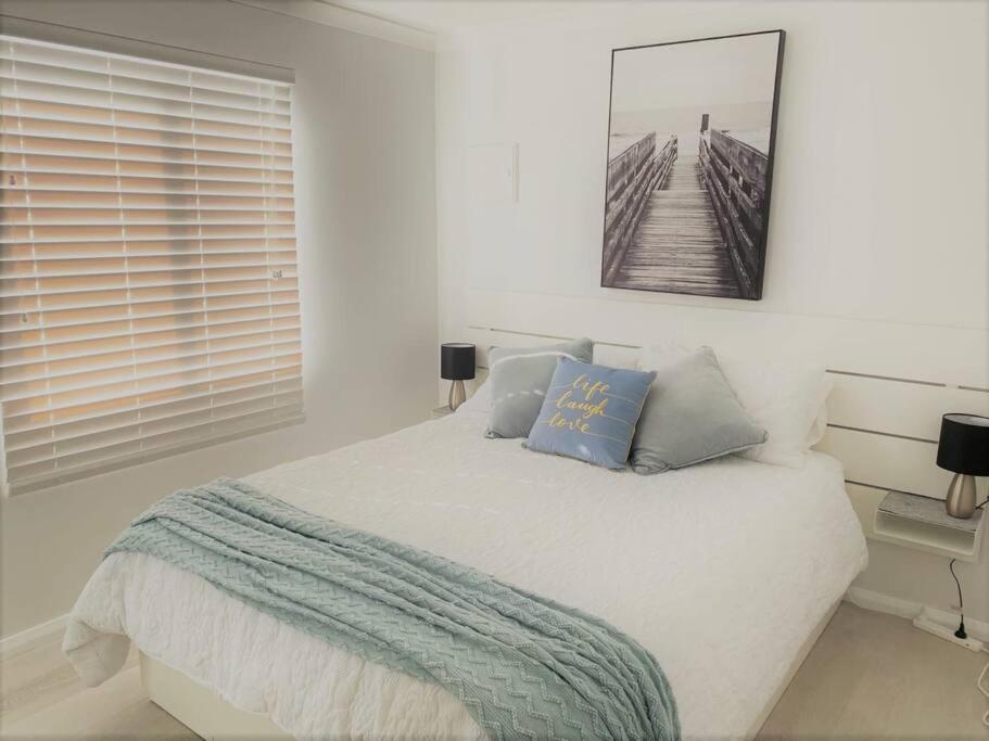 a white bedroom with a bed and a picture on the wall at Salt & Soul Beach Shack in Esperance