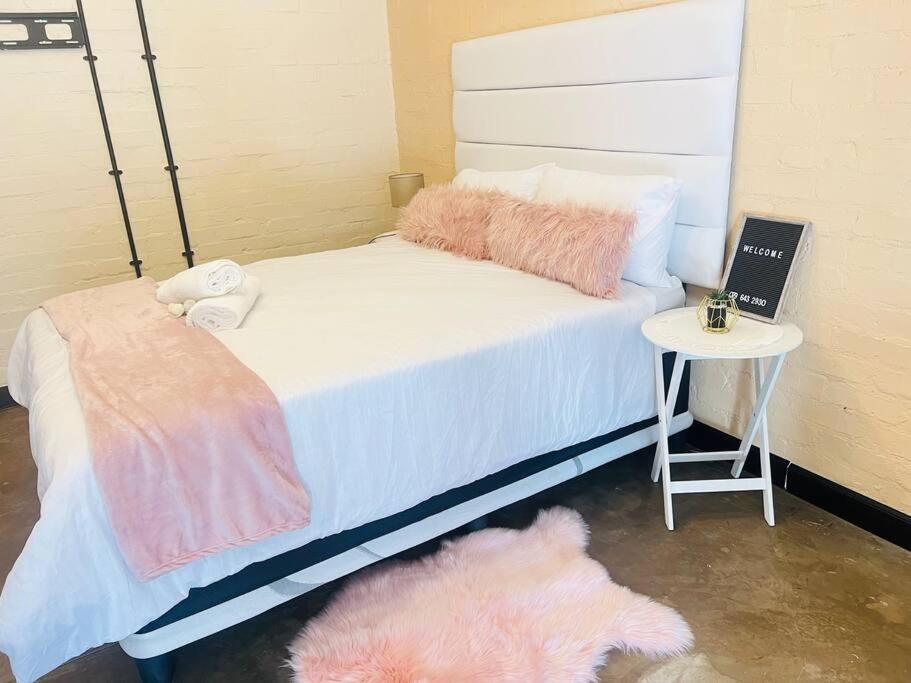 Una cama con almohadas rosas y blancas y una mesa. en Affordable Guest Room @260Main en Johannesburgo