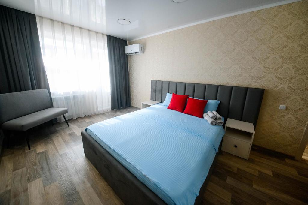 um quarto com uma cama com almofadas vermelhas e uma cadeira em Металлургов 10 em Temirtaū