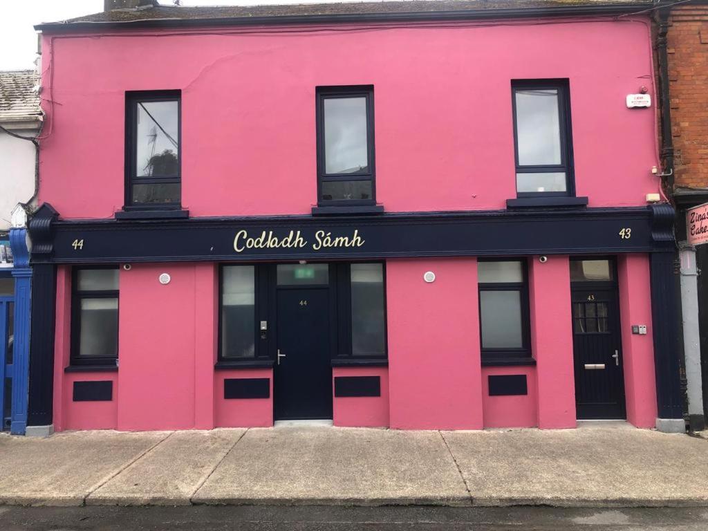 un bâtiment rose avec une porte noire dans une rue dans l'établissement Codladh Sámh, à Templemore