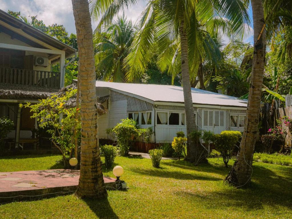 una casa blanca con palmeras en un patio en Villa Tsara - Vacances de rêve à la mer, en Nosy Be