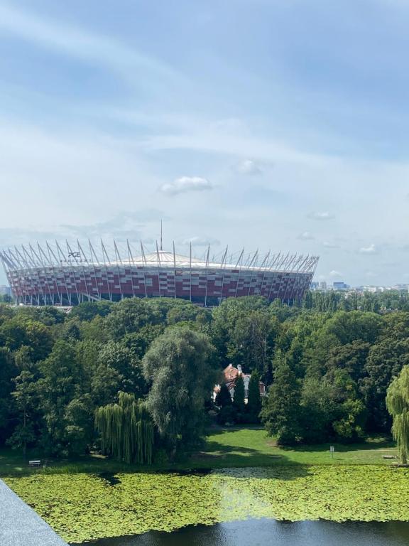 ワルシャワにあるDedek Park - historyczny dworek w pięknym Parku Skaryszewskim obok Stadionu Narodowegoの湖と木々のあるサッカースタジアムの景色