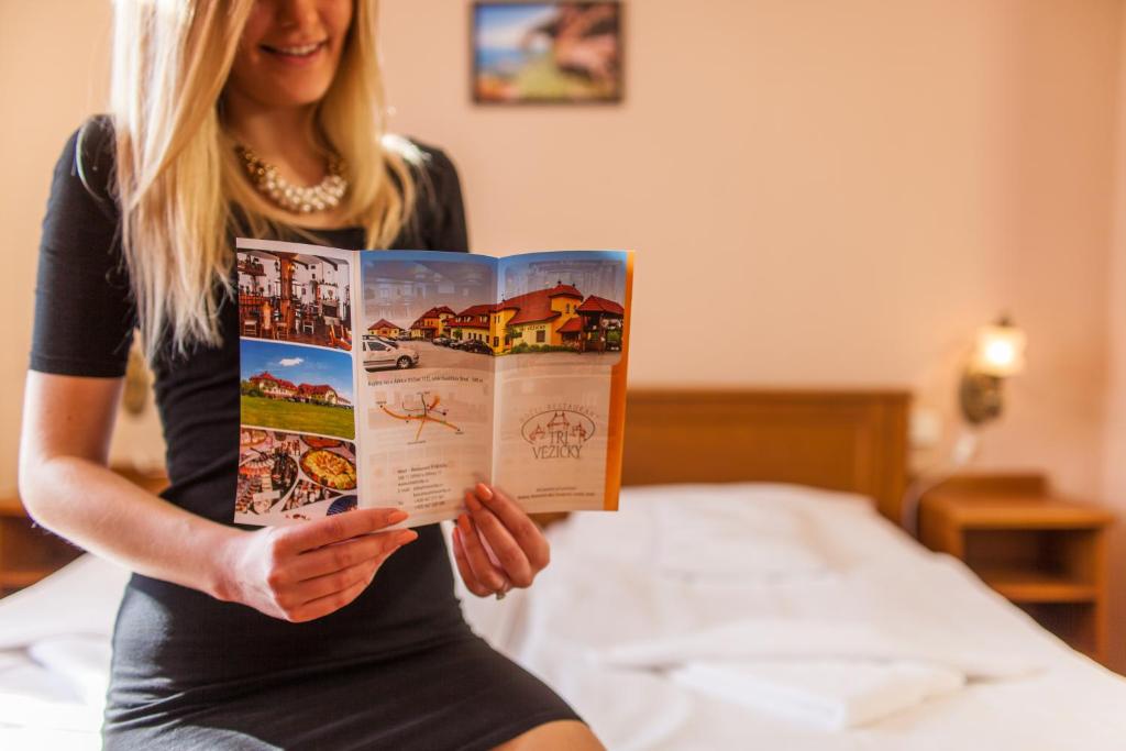 a woman sitting on a bed reading a book at Hotel Tři Věžičky in Střítež