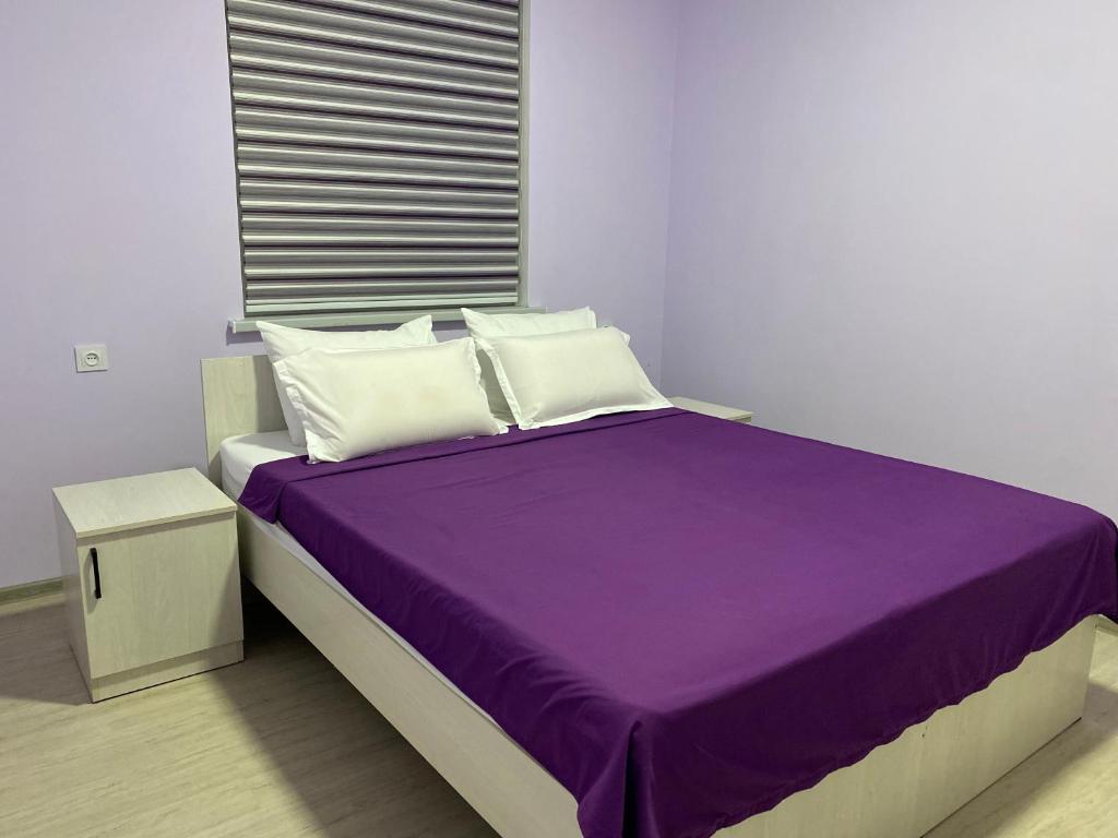 a bed with purple sheets and white pillows in a room at Apart House in Türkistan