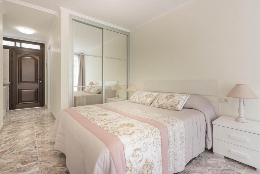 a white bedroom with a bed and a mirror at TENERIFE Olympia Apart Hotel-Playa de las Americas. Balcony, sea view & pool in Playa de las Americas