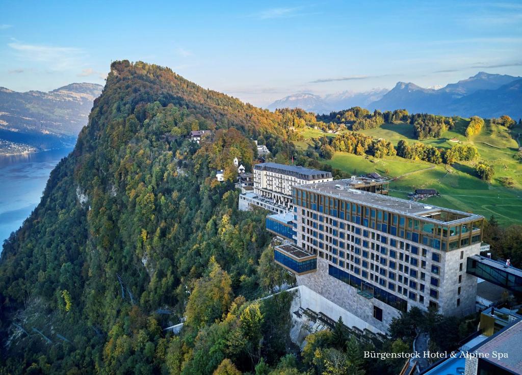 een gebouw aan de zijkant van een heuvel met bomen bij Bürgenstock Hotel & Alpine Spa in Bürgenstock