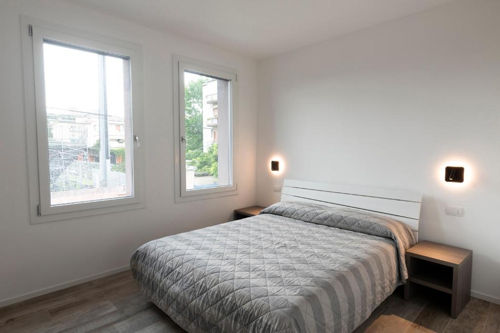 a white bedroom with a bed and two windows at Residence Cavalli in Mestre