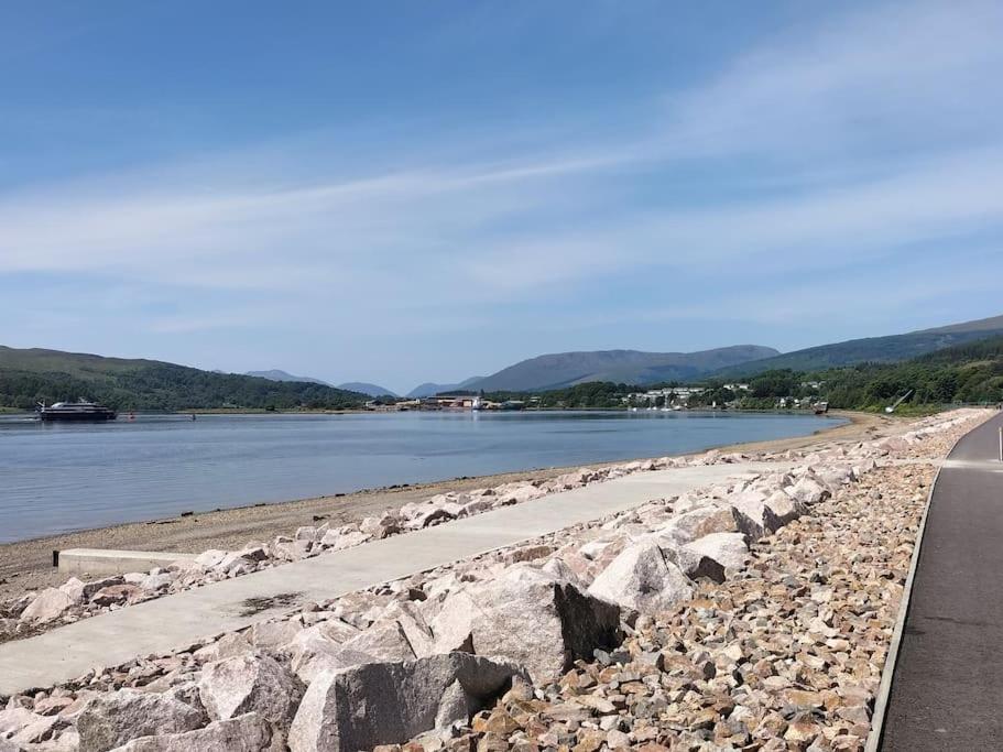 a road next to a body of water with rocks at A view to Caol, Fort William in Fort William