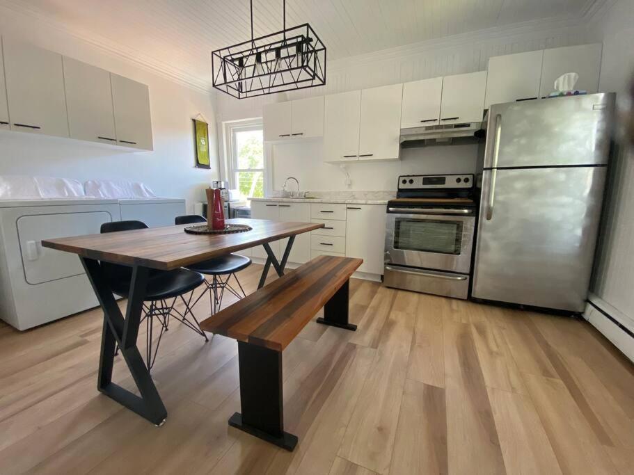 a kitchen with a table and a stainless steel refrigerator at Logement au Cœur du Village in Saint-Jean-Port-Joli