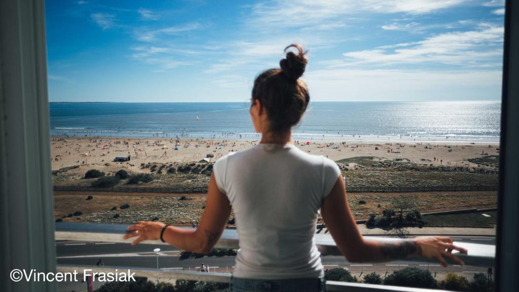 een vrouw die uit een raam naar het strand kijkt bij Hôtel Spa du Beryl Joa in Saint-Brevin-les-Pins