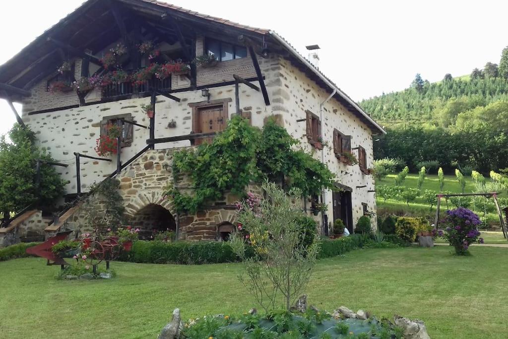 un gran edificio de piedra con flores delante en caserio vasco con piscina y barbacoa, en Murueta-Orozko