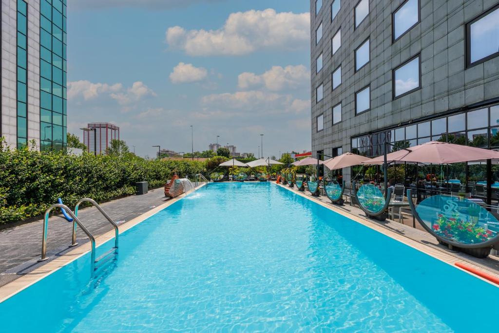 ein großer Pool mit Stühlen und Sonnenschirmen neben einem Gebäude in der Unterkunft iH Hotels Milano Lorenteggio in Mailand