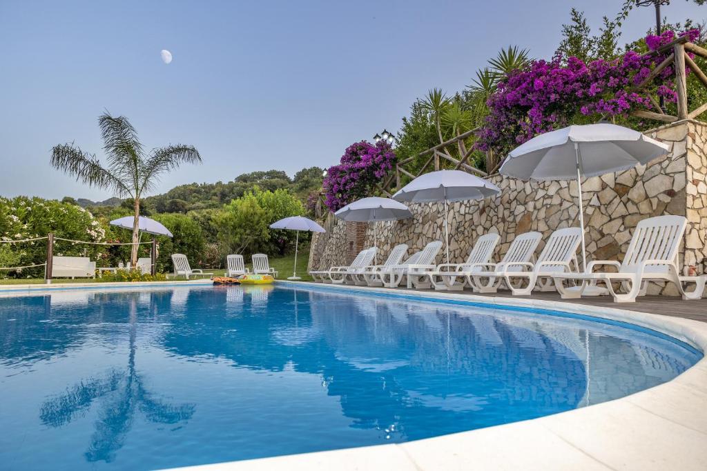 una piscina con sillas y sombrillas blancas en Arcaloro Resort, en SantʼAngelo di Brolo