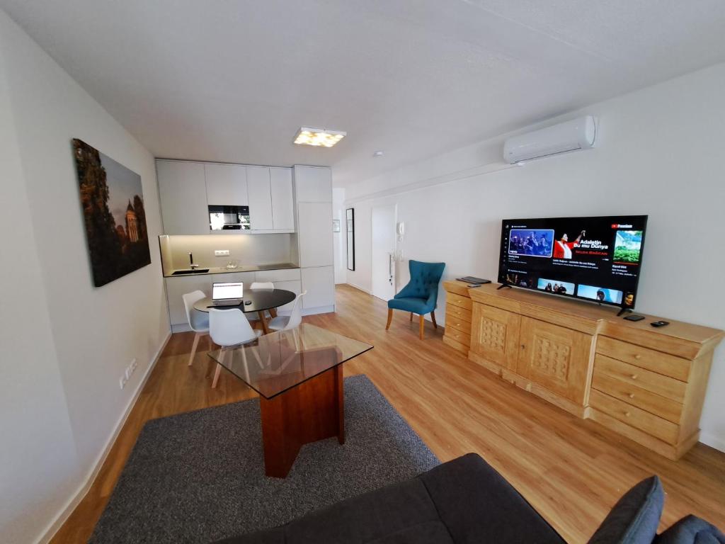 ein Wohnzimmer mit einem TV, einem Tisch und Stühlen in der Unterkunft East Park Apartments Baumkirchner Str 18 in München
