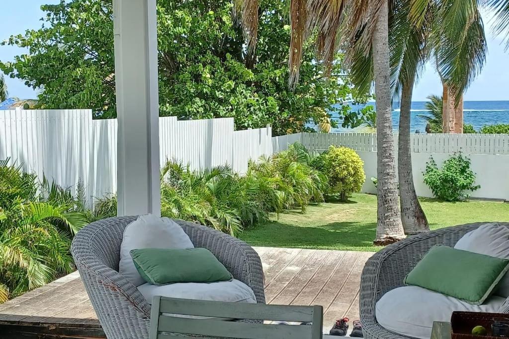 a porch with two wicker chairs with green pillows at Un cocon les pieds dans l'eau in Le Moule