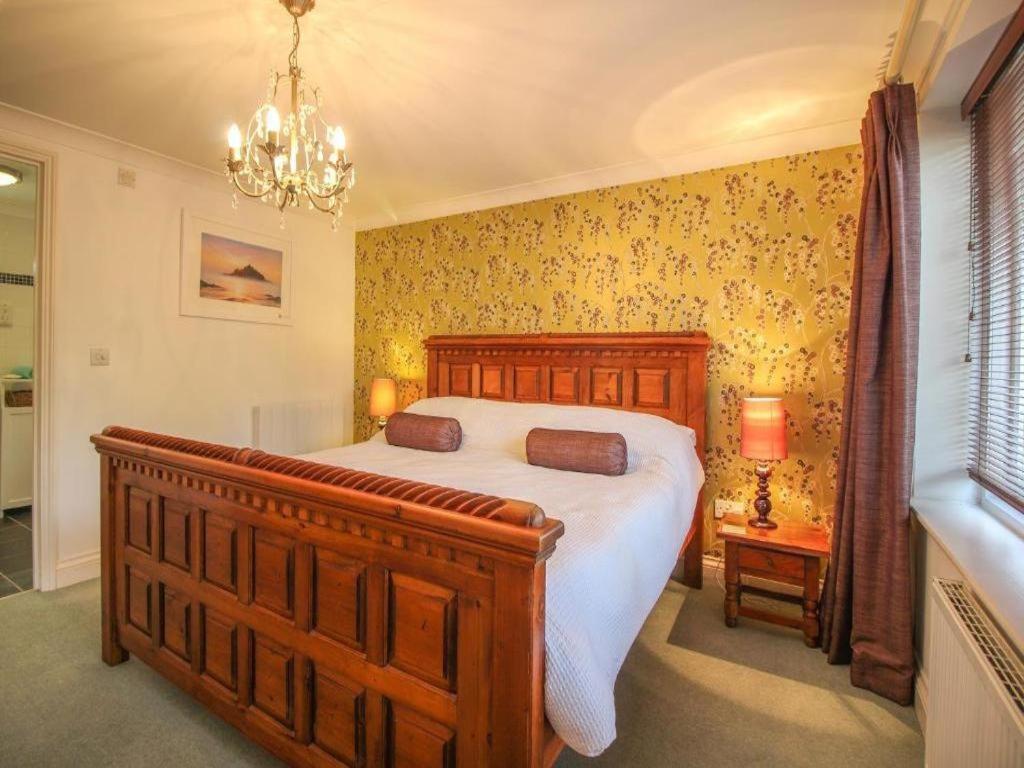 a bedroom with a wooden bed and a chandelier at Dune Cottage sleeps 2 with parking pet friendly close to St Ives & Penzance in Saint Erth