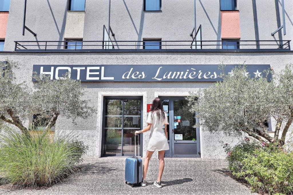 een vrouw met een koffer voor een hotel des lumes bij Hôtel des Lumières Lyon Meyzieu Arena Stadium in Meyzieu