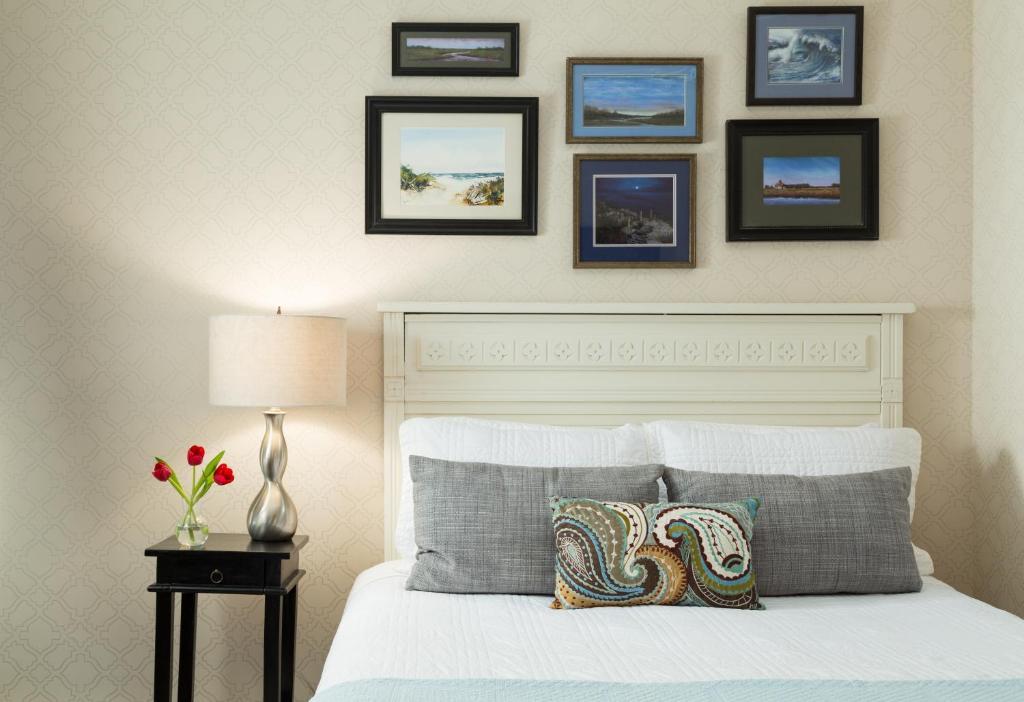 Un dormitorio con una cama blanca con cuadros enmarcados en la pared en The Carroll Villa Hotel, en Cape May