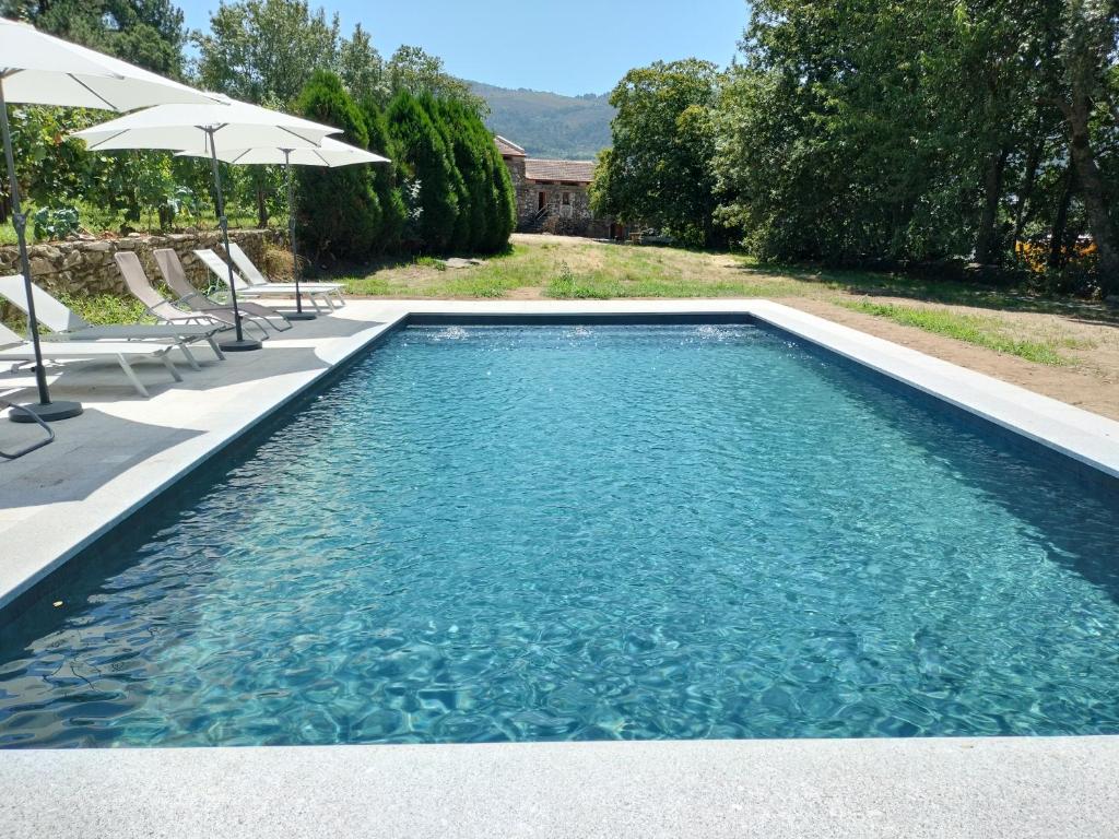a swimming pool with blue water and umbrellas at Casa das Bouças in Melgaço