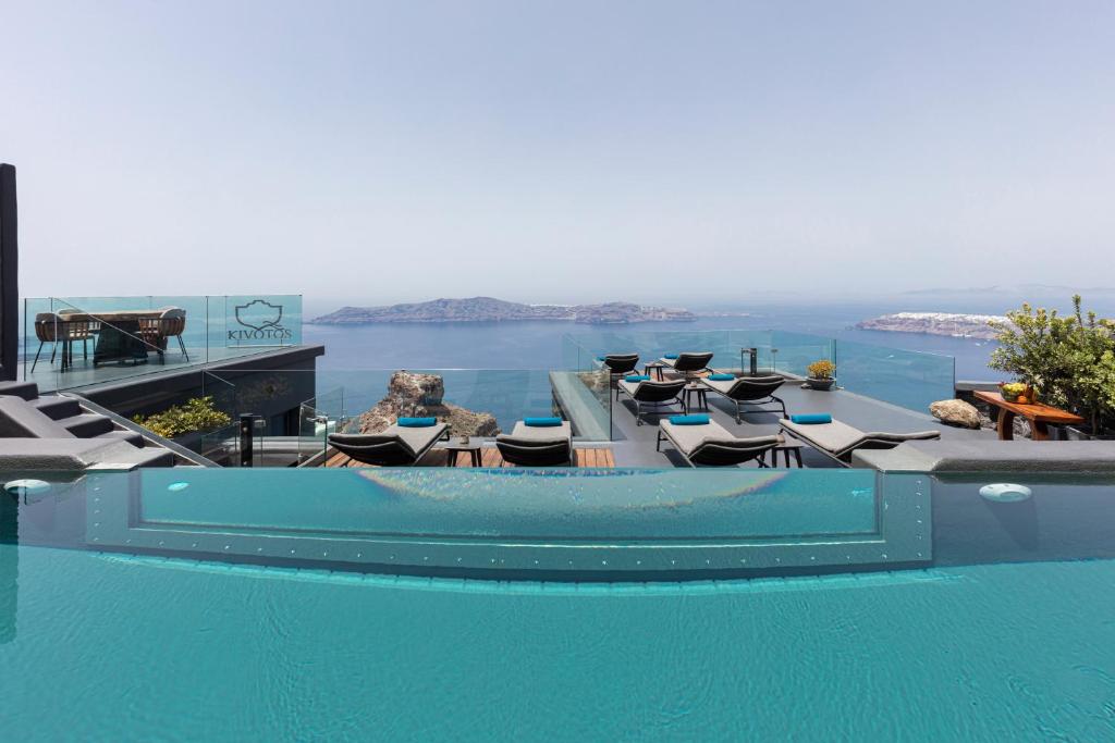 a swimming pool with chairs and a view of the ocean at Kivotos Santorini in Imerovigli