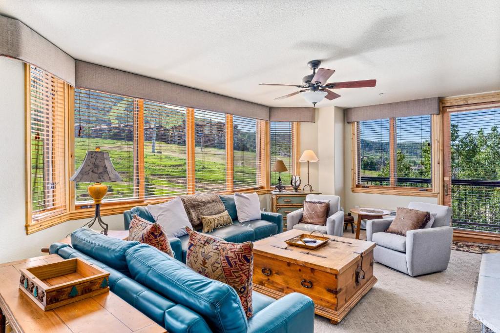 uma sala de estar com um sofá azul, cadeiras e janelas em Torian Plum Creekside 513 em Steamboat Springs