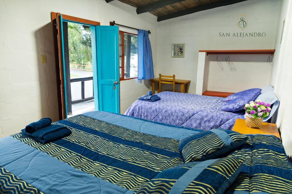 a bedroom with two beds with blue sheets and a window at Finca San Alejandro in Cotacachi